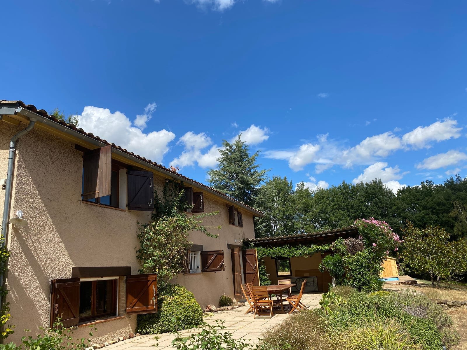 La façade aux volets bois, la terrasse et le jardin fleuri